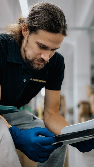 Warehouse employee wearing gloves and focusing on a tablet screen for quality check.